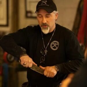 A man in black shirt and hat holding a knife.