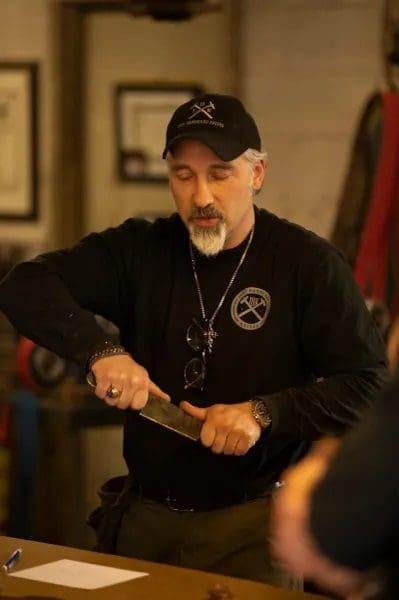 A man in black shirt and hat holding a knife.